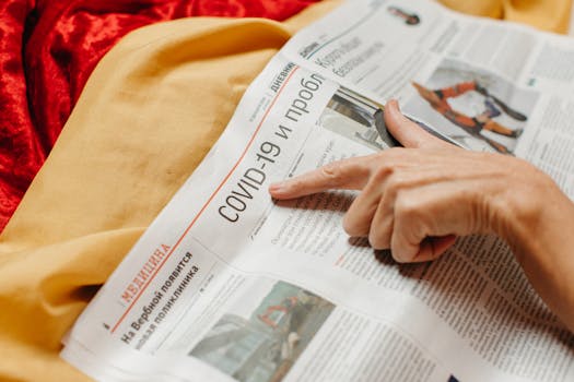 A close-up shot of a hand pointing at a COVID-19 headline in a newspaper.